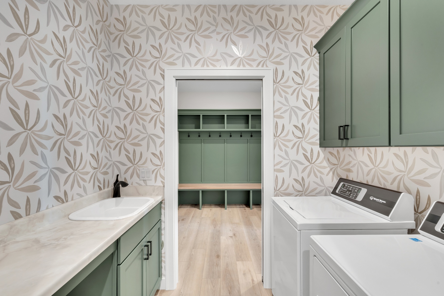 Laundry room with botanical wallpaper and green cabinetry
