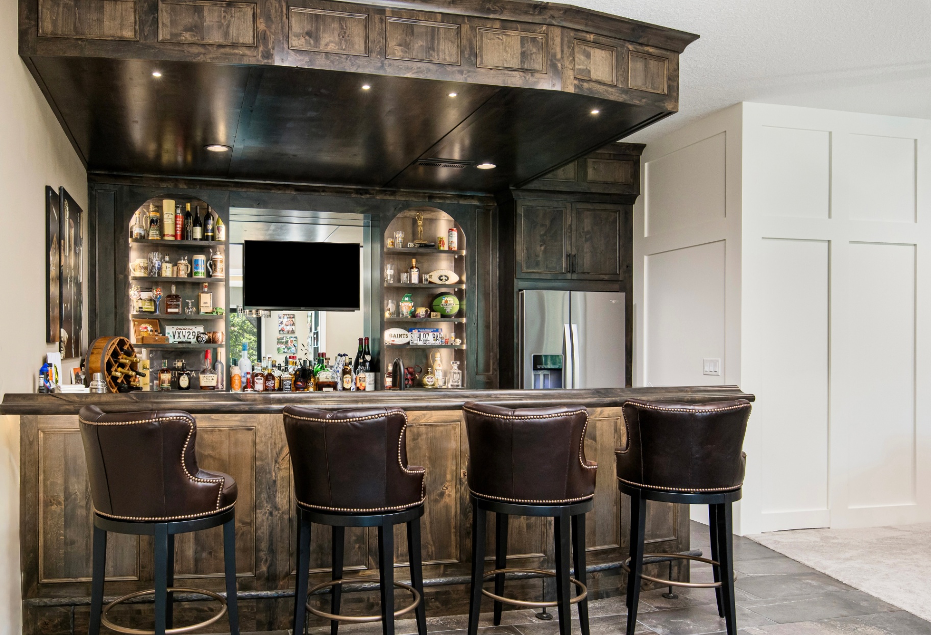 Custom lower-level bar with dark wood cabinetry and leather stools