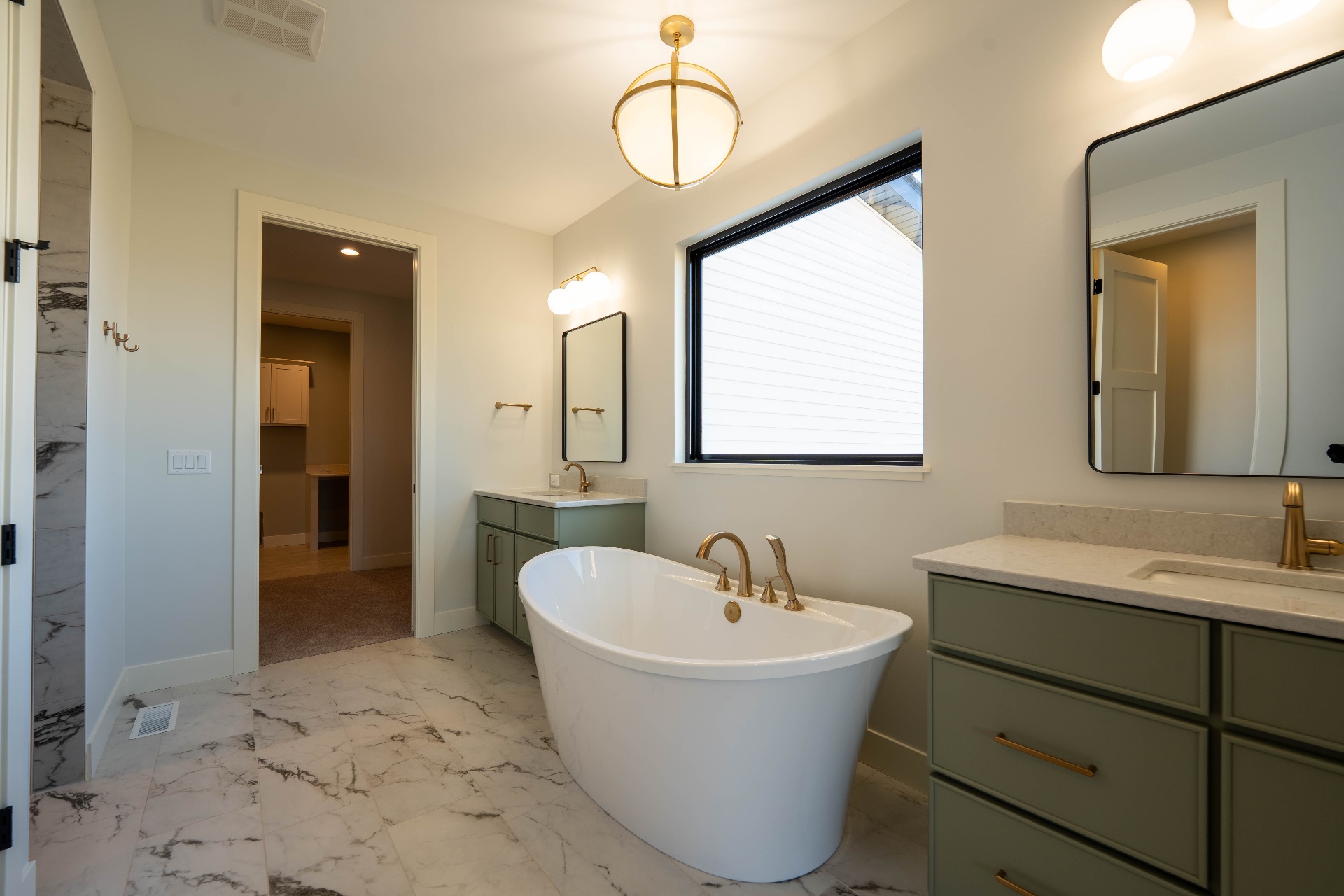 Primary bath with freestanding tub, sage vanities, and brass fixtures